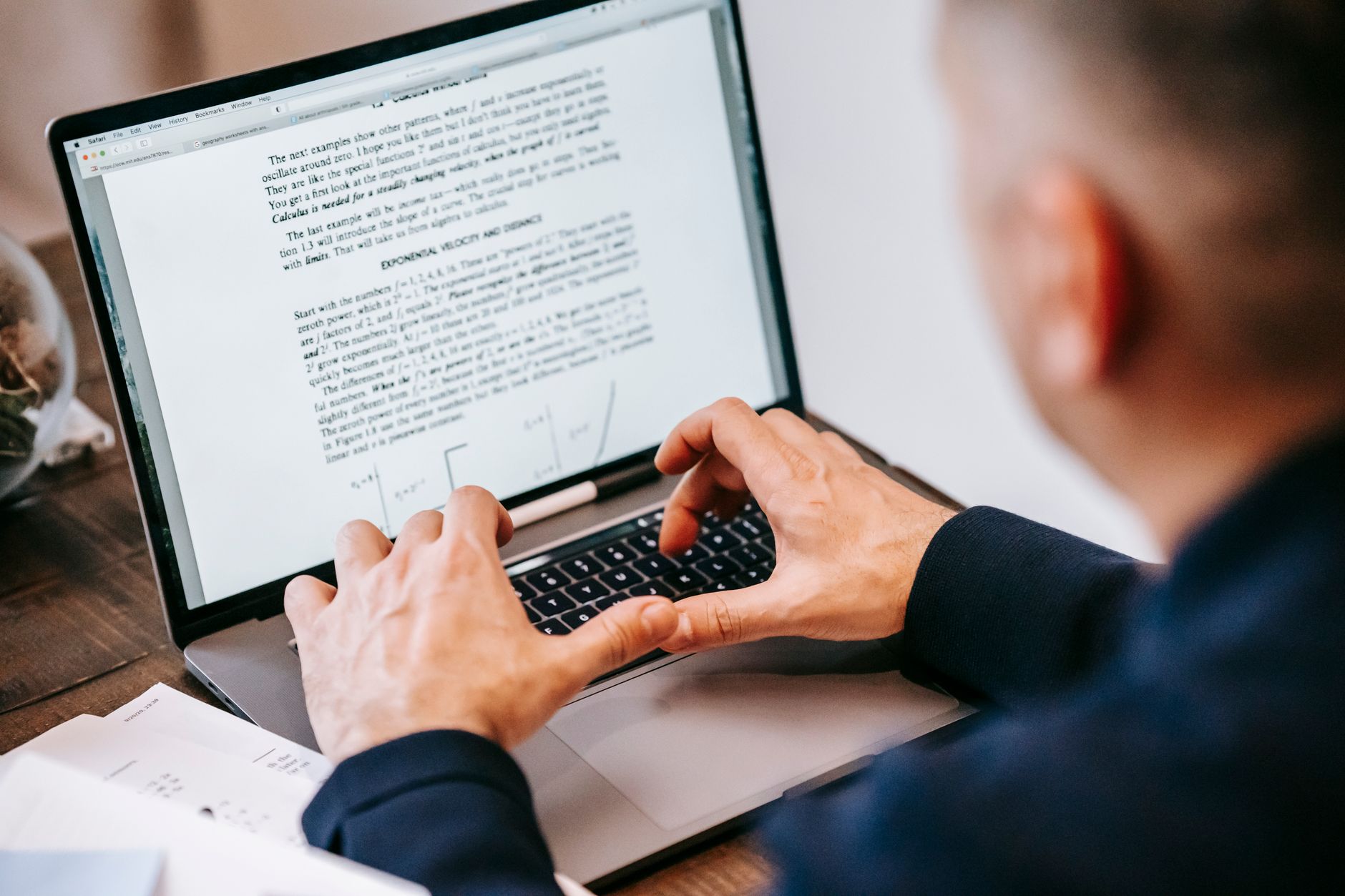 A person types on a laptop showing a document with text and equations