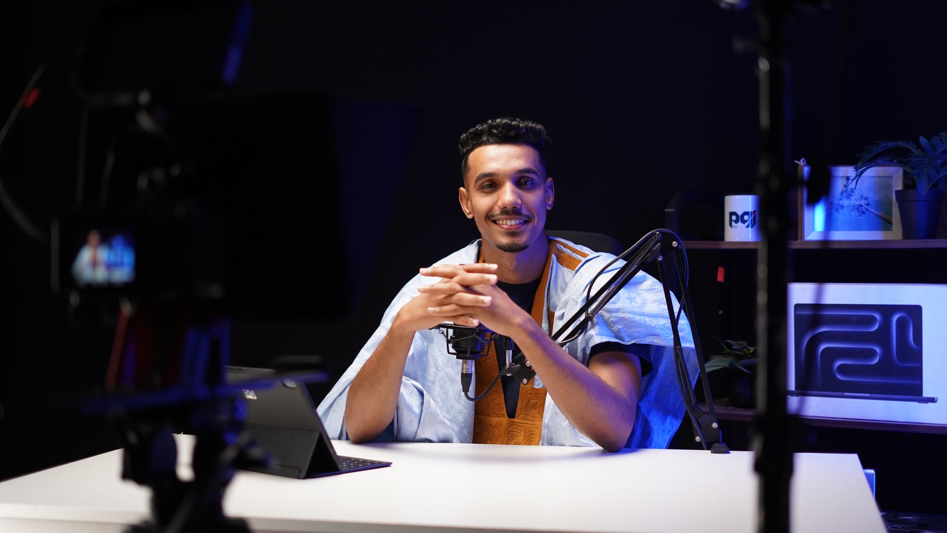 Smiling podcaster with mic, camera, and tablet recording new content in a studio