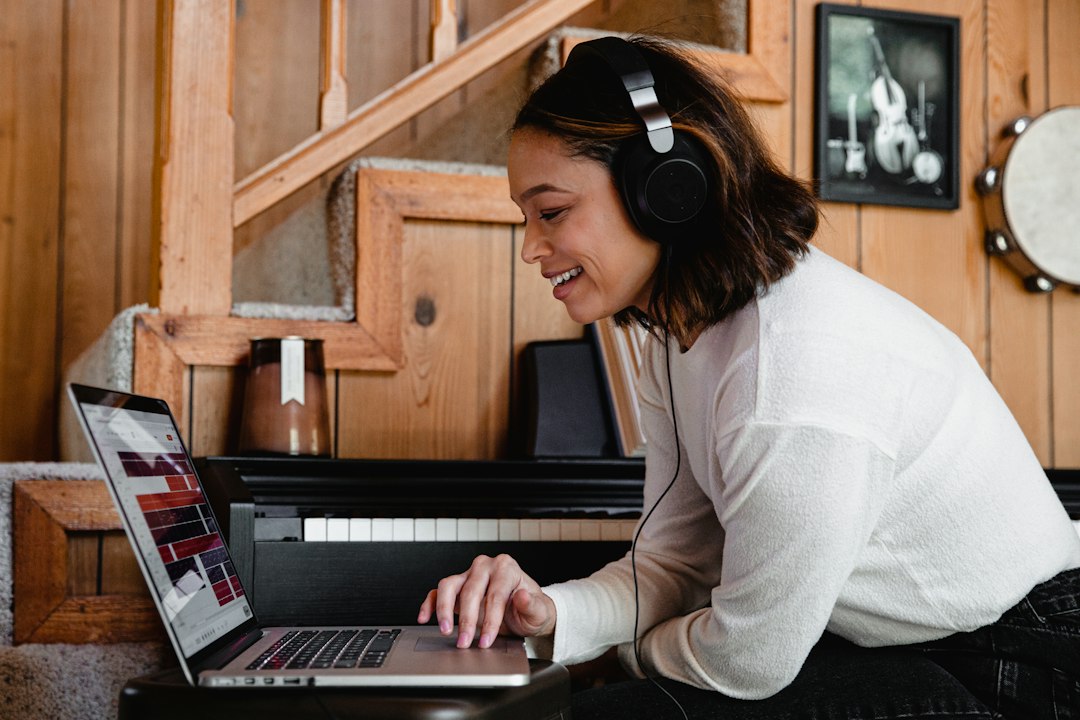 A smiling woman wearing headphones looks at a laptop beside a piano