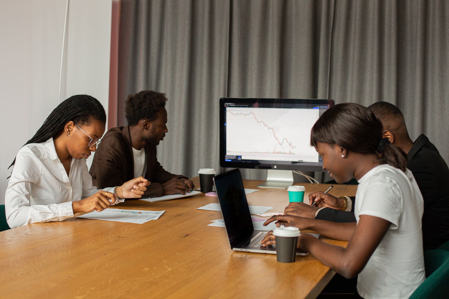 Four professionals analyzing data on laptops and a monitor at a conference table