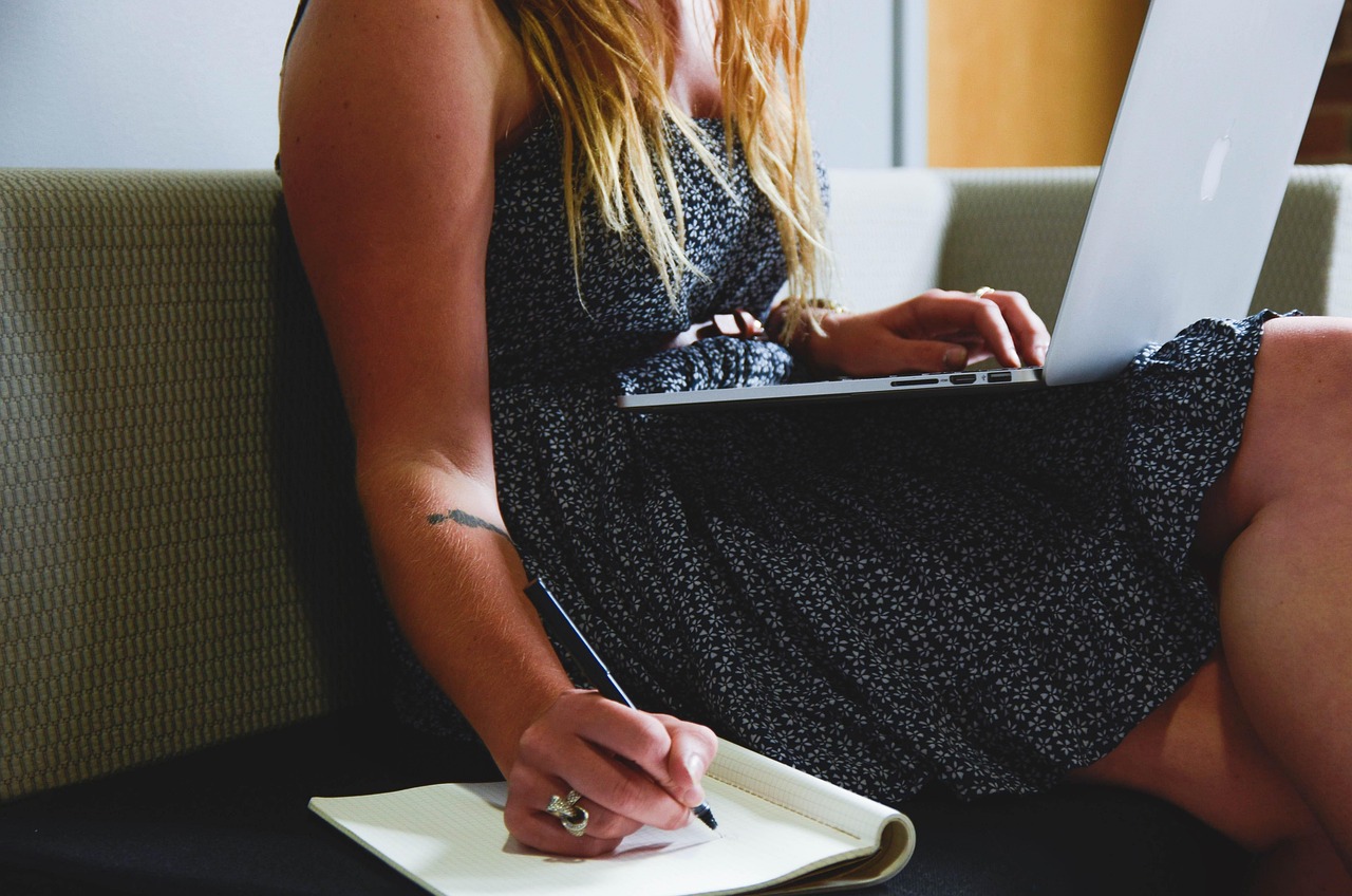 Woman in floral dress taking notes while working on a laptop computer