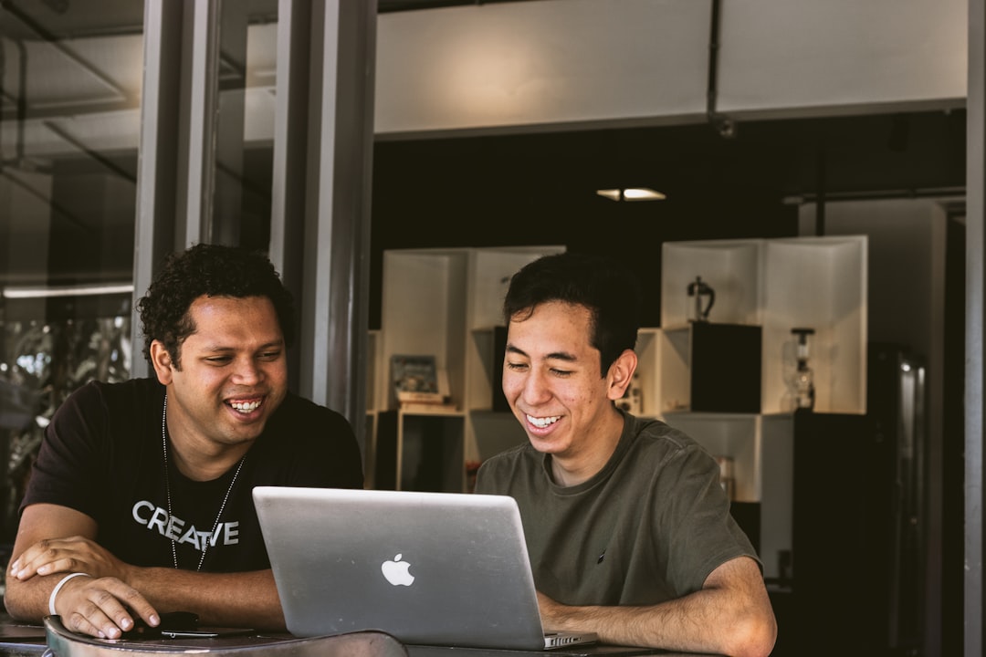 Two smiling men collaborate on a laptop, discussing automated SEO services