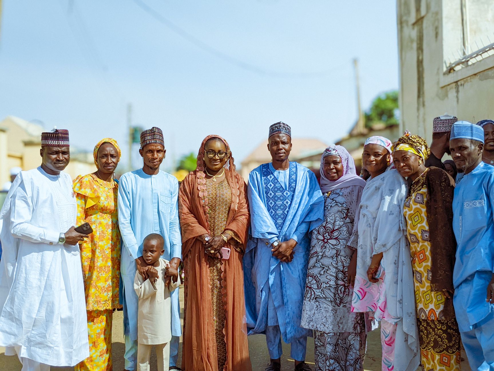 A diverse group of people in colorful traditional clothing standing outdoors, smiling