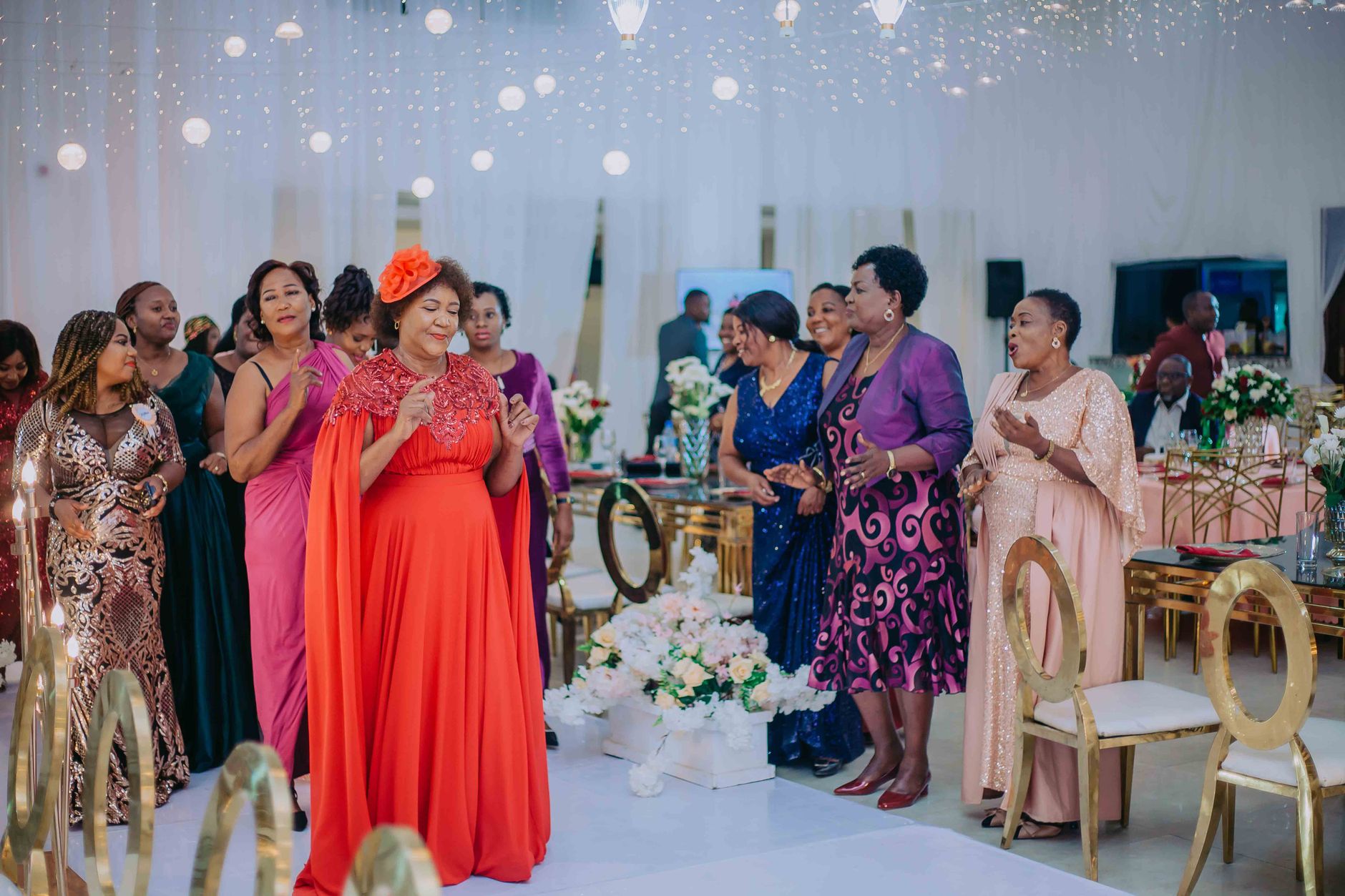 Women in vibrant formal wear enjoy an event under sparkling lights and elegant decor