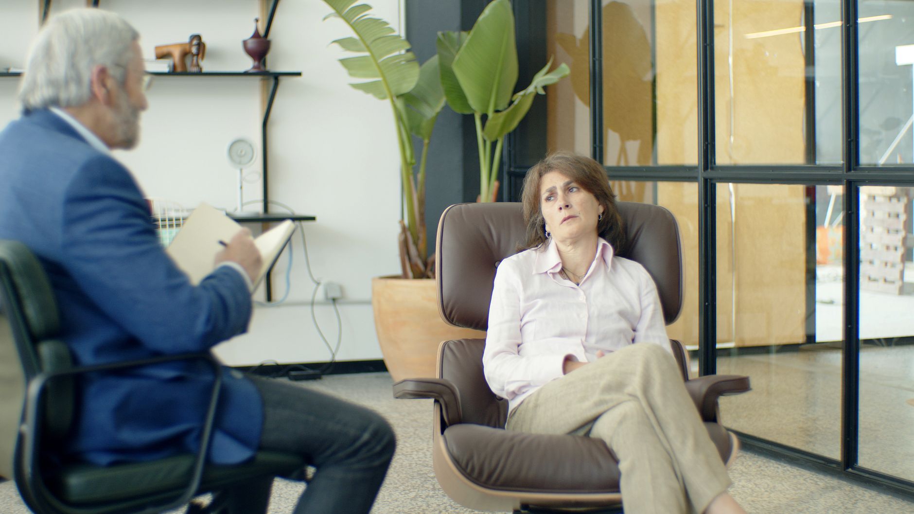 Woman in therapy session looking thoughtful while a male therapist takes notes