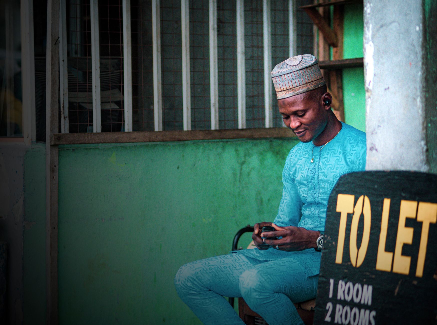 Man in traditional attire sits beside a "TO LET" sign in Lagos