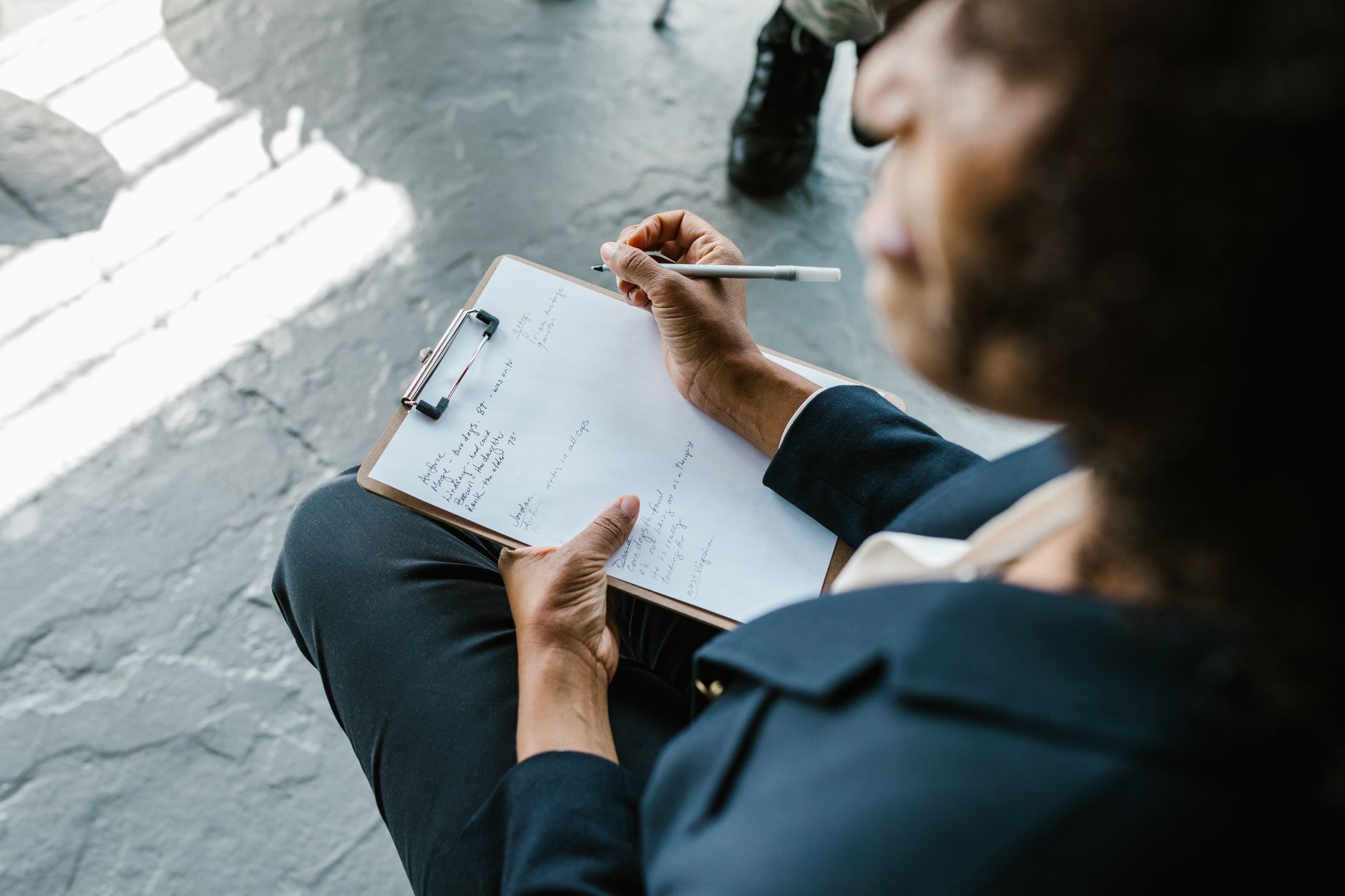 Person in dark clothing writing notes on a clipboard with a pen