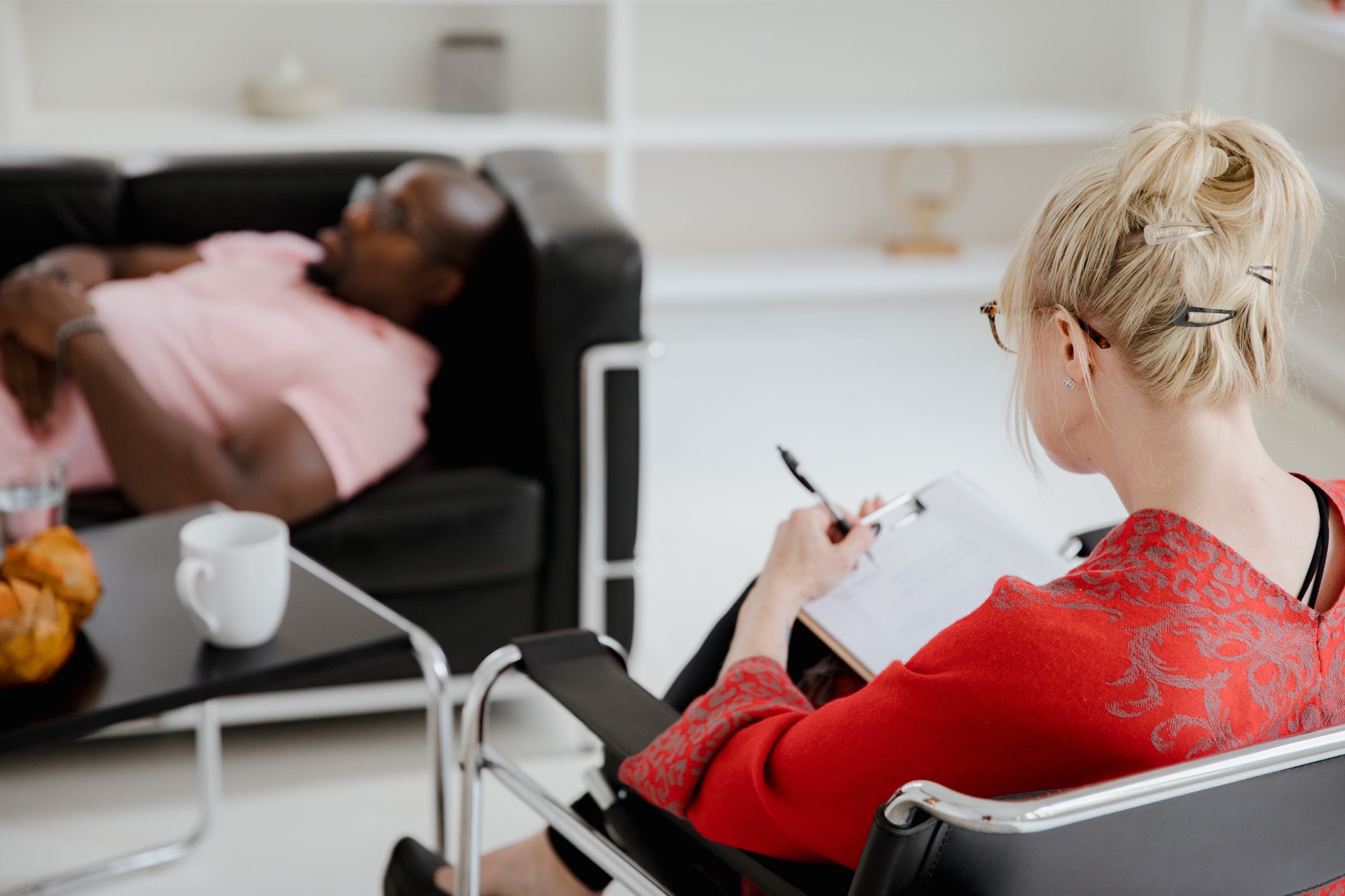 A therapist takes notes while a patient lies on a couch in a therapy session
