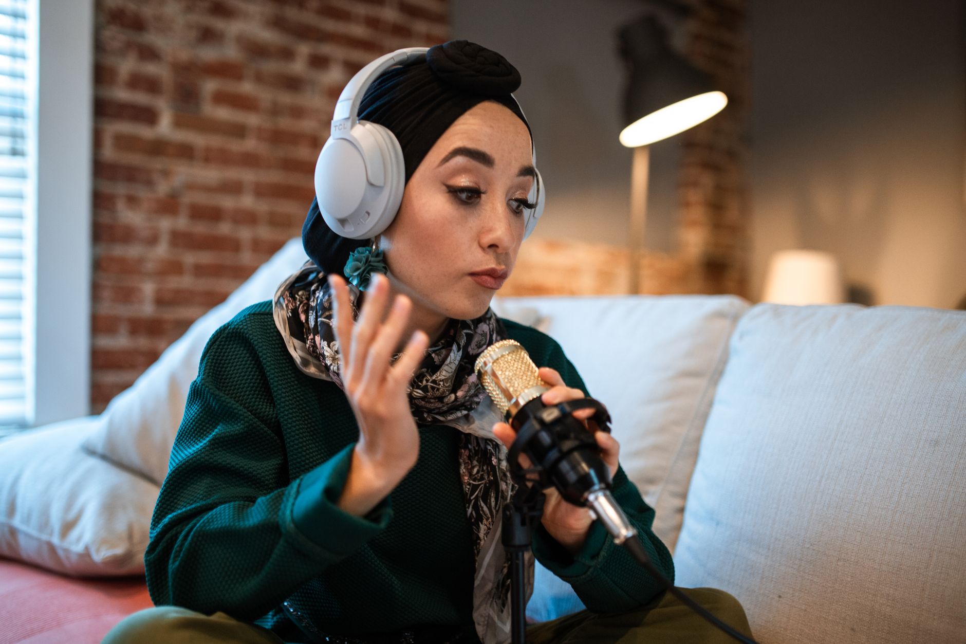 Woman with white headphones and turban recording a podcast into a gold microphone