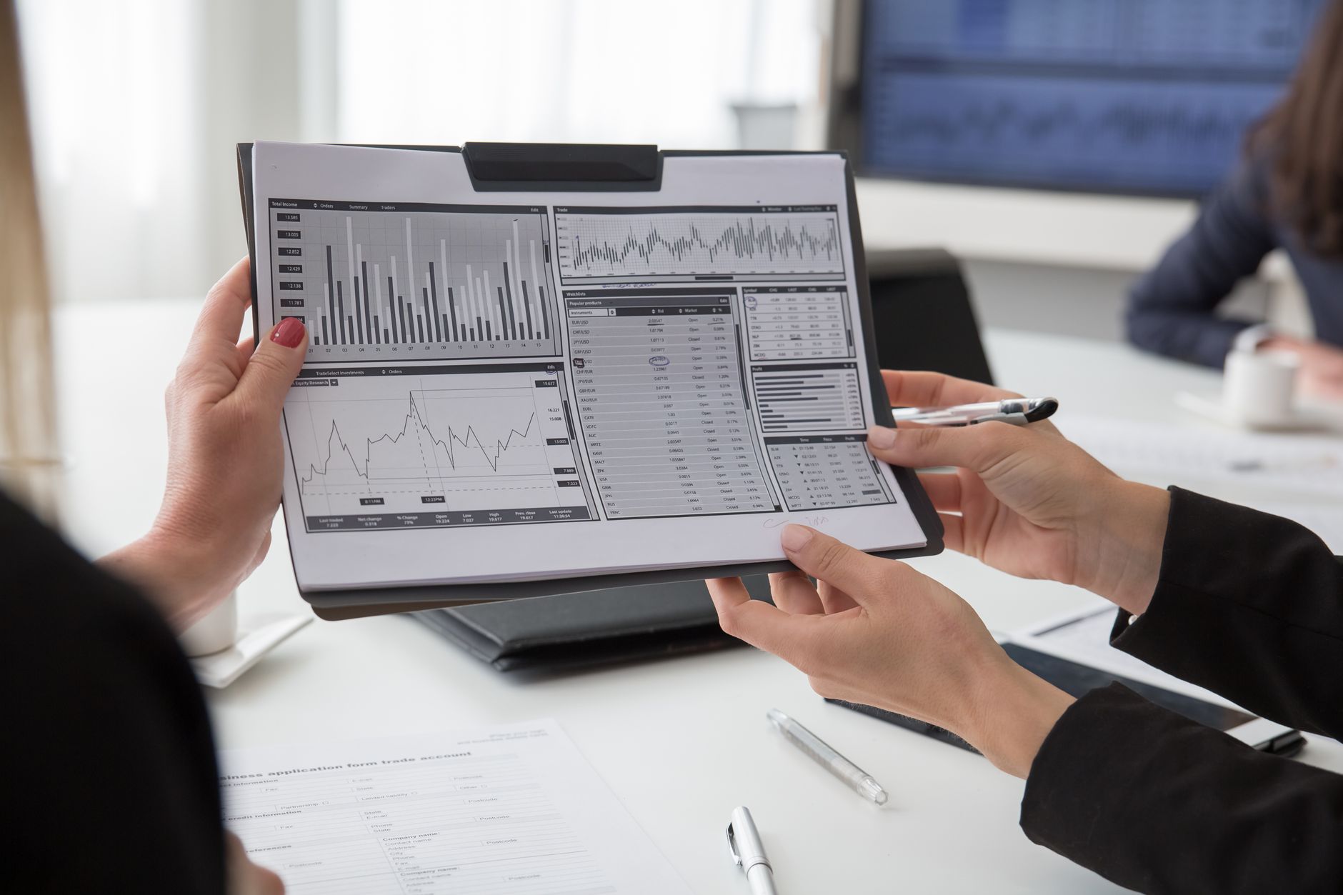 Two people's hands hold a clipboard showing charts and graphs for analysis
