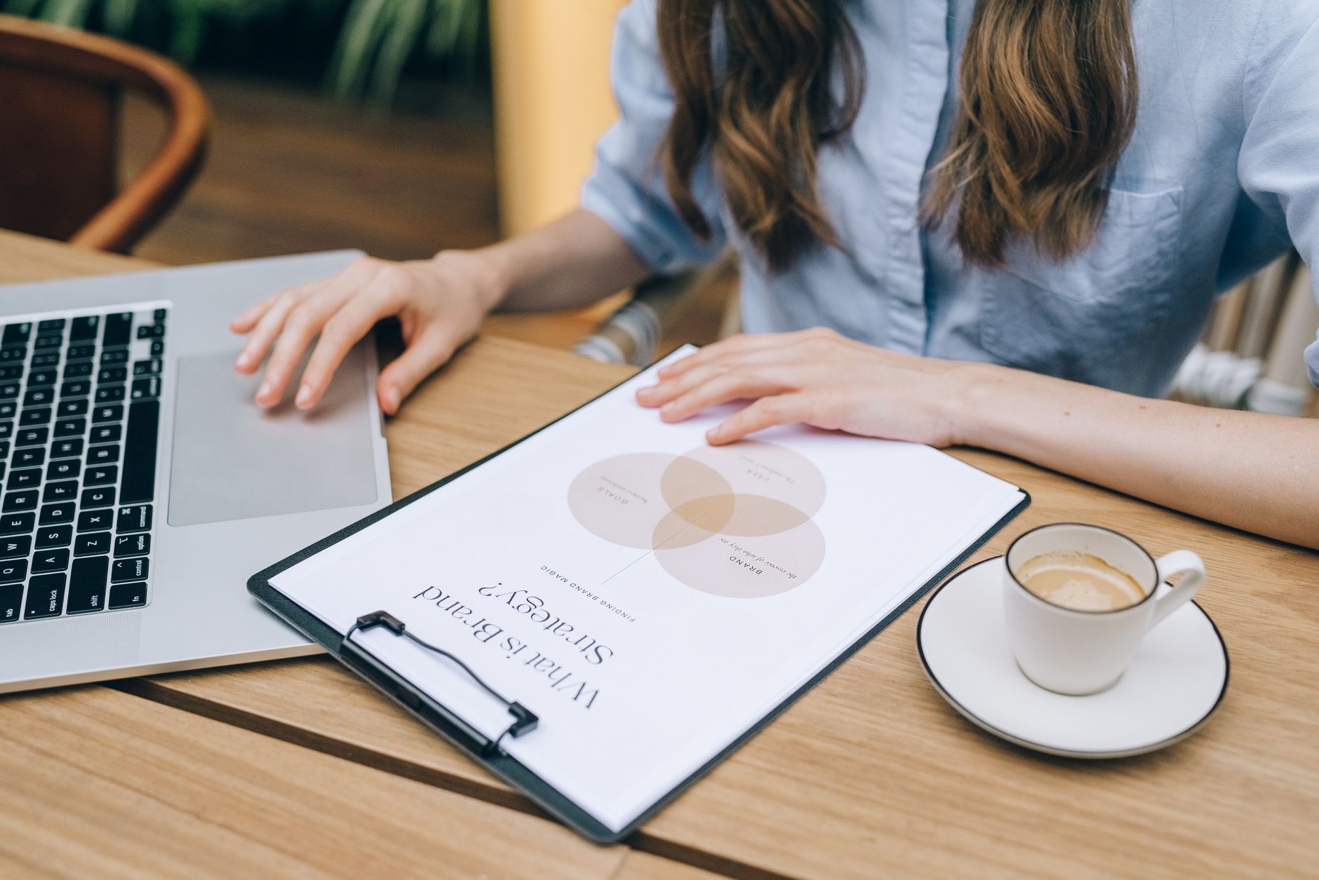 Person's hands working on a laptop with a brand strategy document and coffee