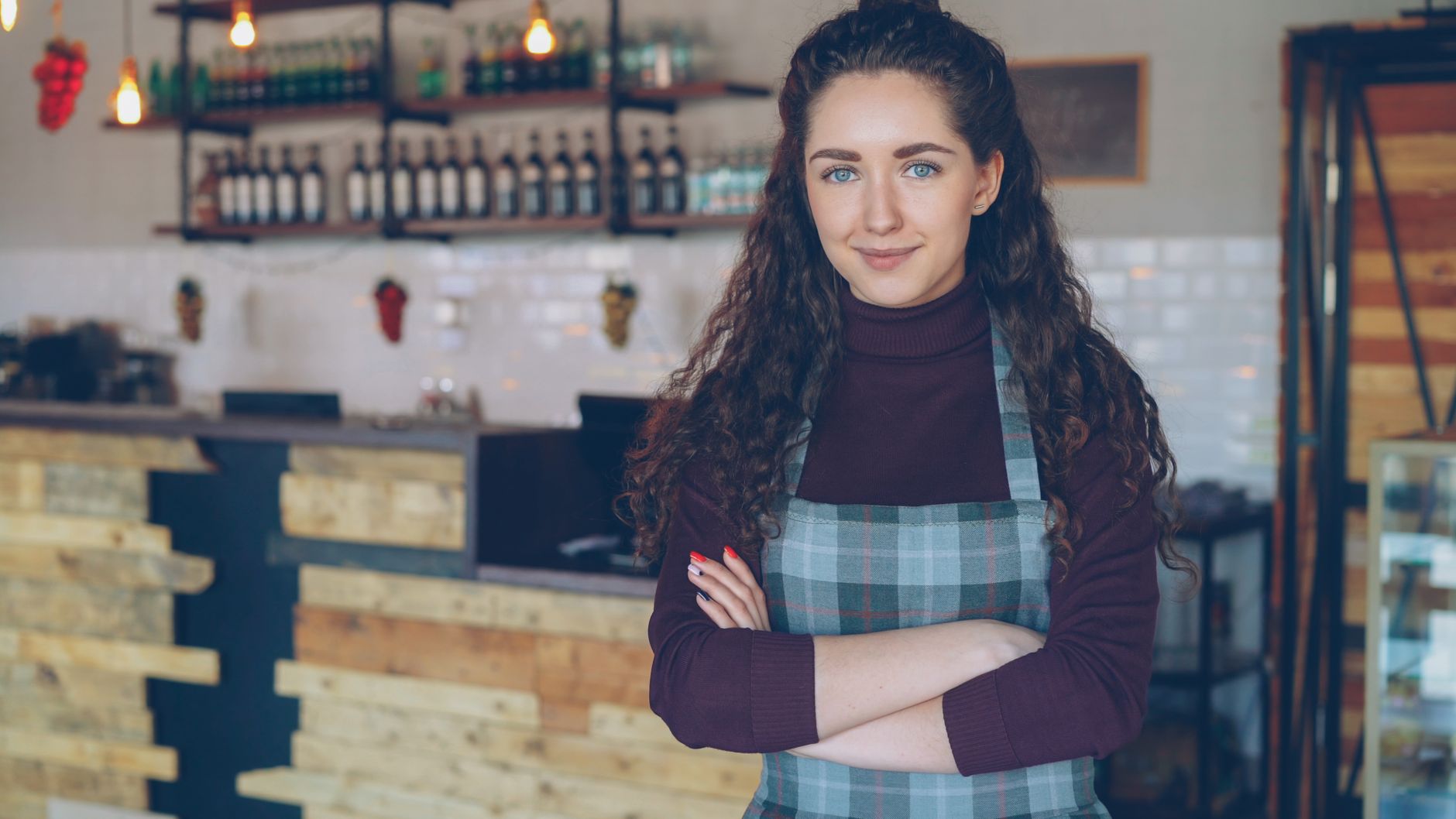Smiling small business owner wearing an apron, arms crossed, standing in a shop