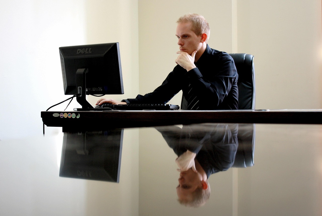 Man intently thinking while working on a computer at a glossy desk