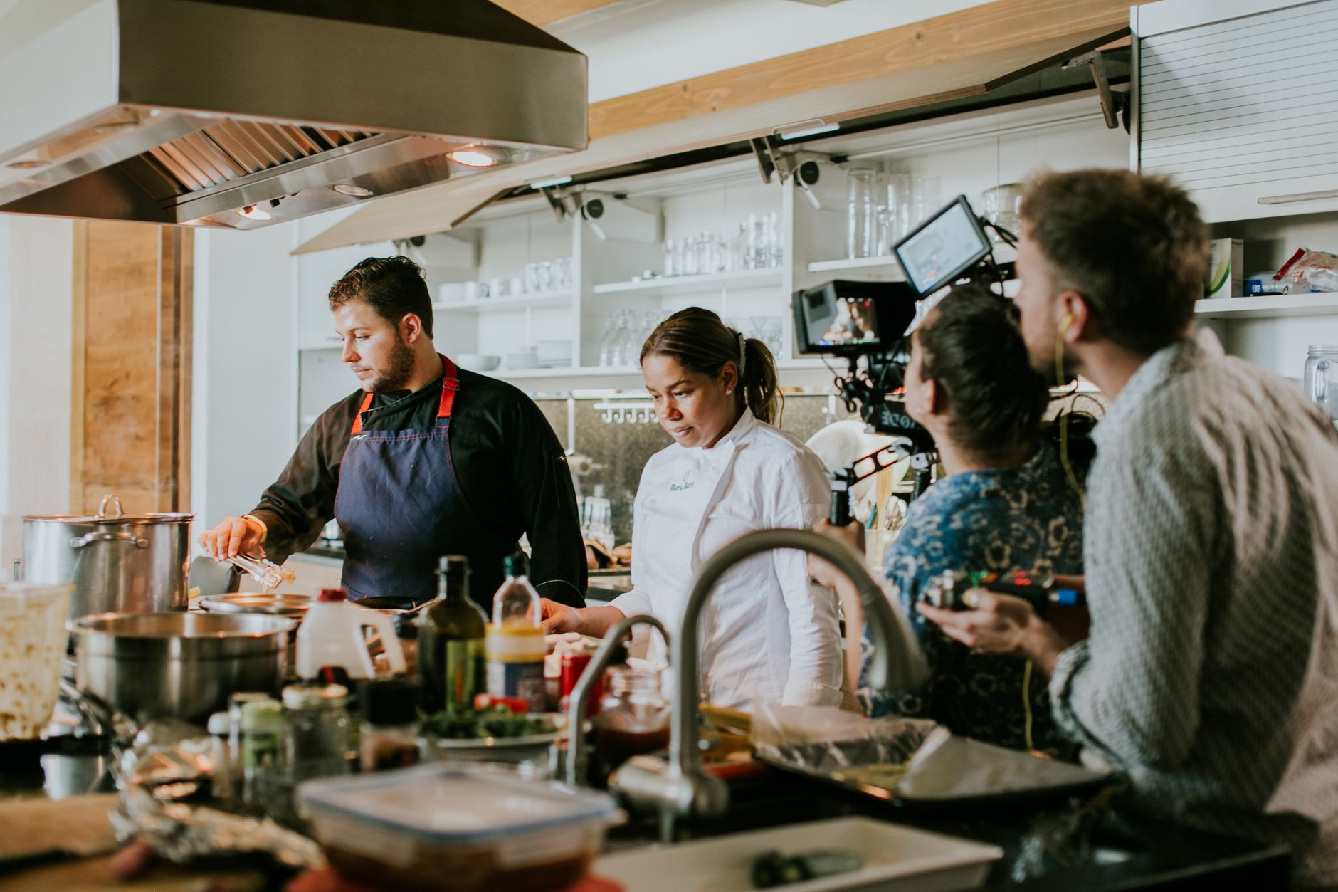 Two chefs cooking in a commercial kitchen with people observing, like a catering team