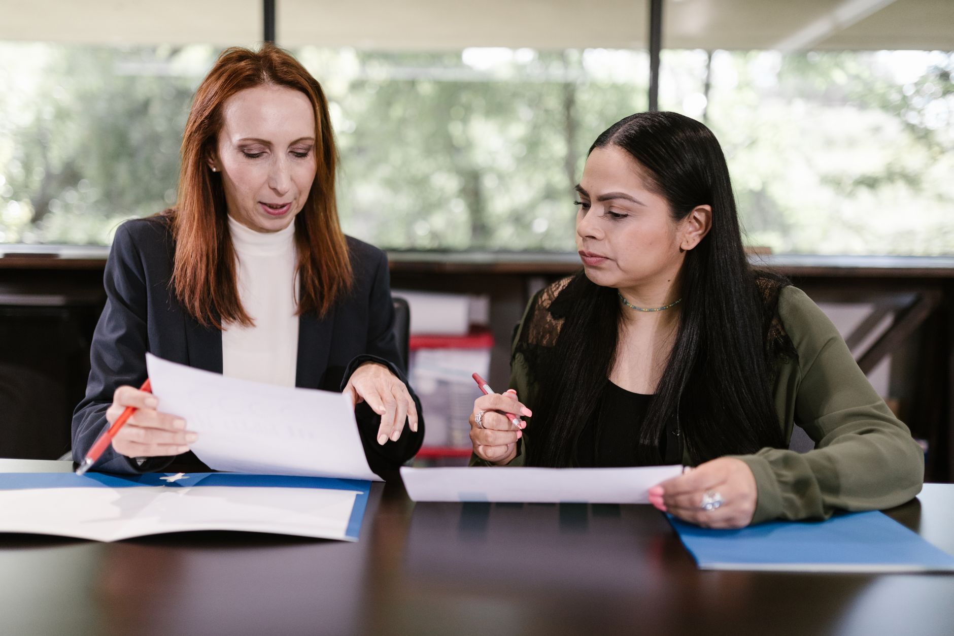 Two women reviewing documents and discussing catering budget details at a table