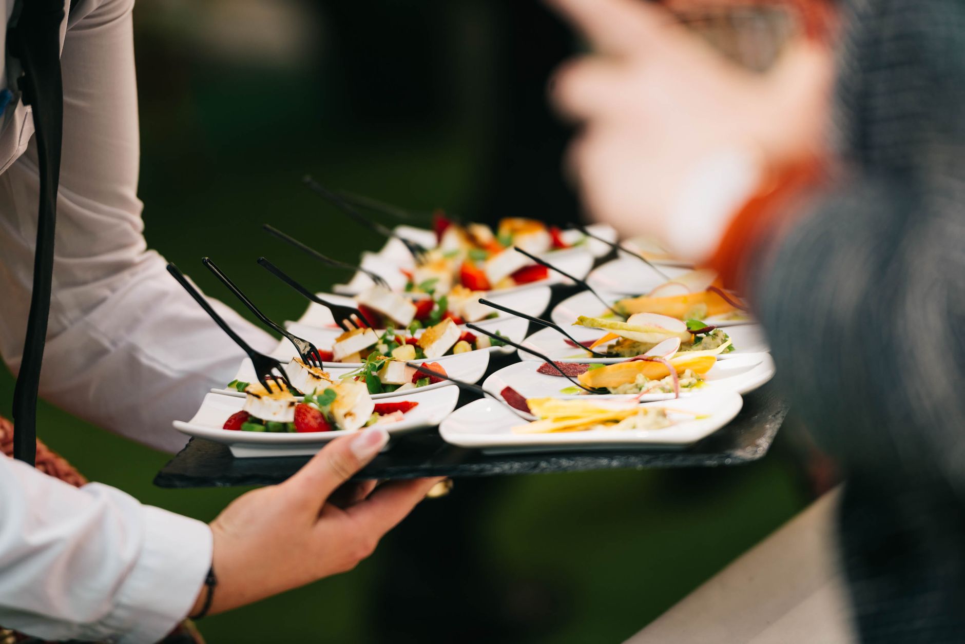 Caterer serving a tray of gourmet appetizers on small plates with forks
