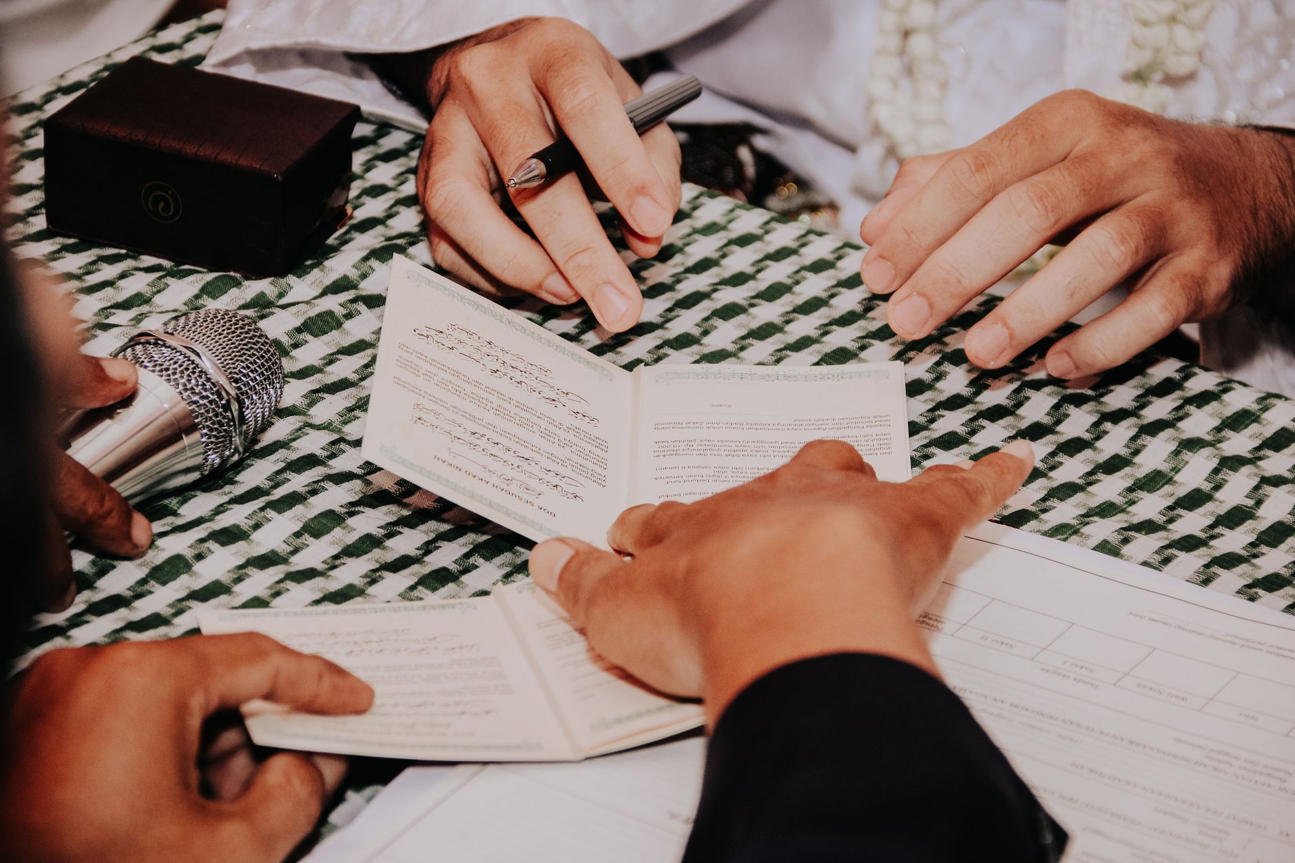 Hands of individuals signing or reviewing documents with a pen and microphone nearby
