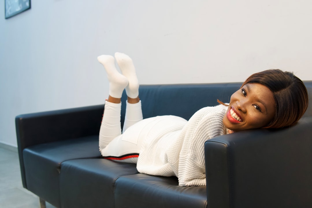 Smiling woman in white relaxes on a black couch with feet up