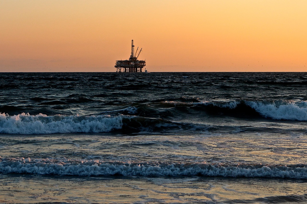 Oil rig on dark ocean waves under an orange sunset sky