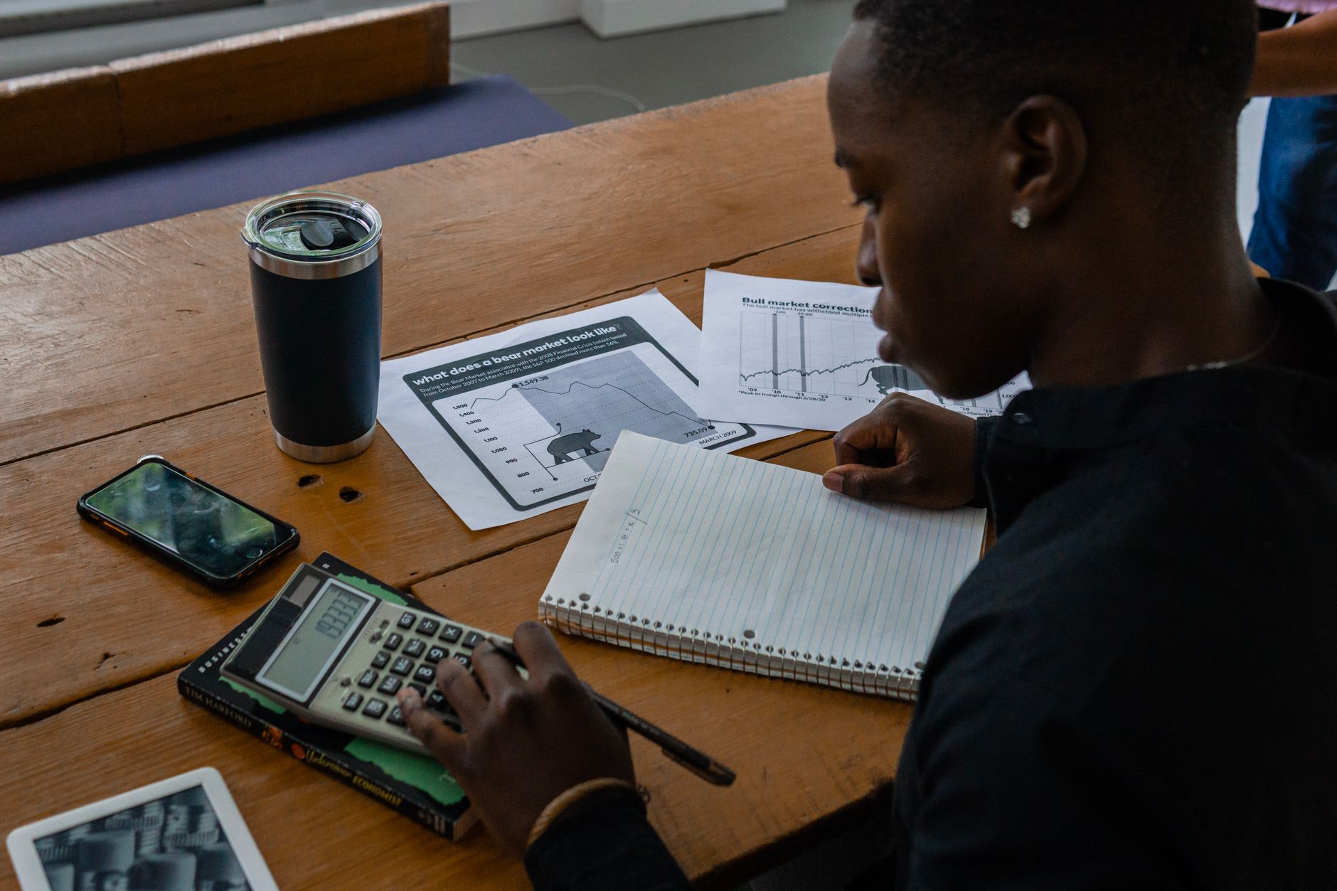 Person using a calculator, notebook, and financial charts for business analysis