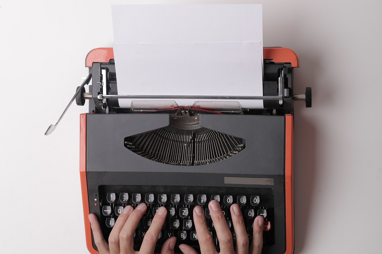 Hands typing on a vintage typewriter with blank paper, representing content creation