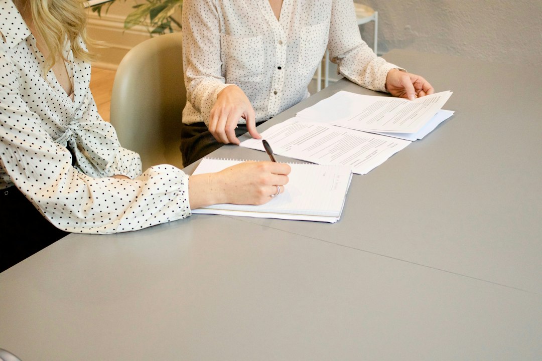 Two people discussing documents at a table, one taking notes