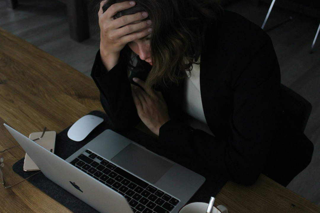 A woman rests her hand on her forehead above an open laptop
