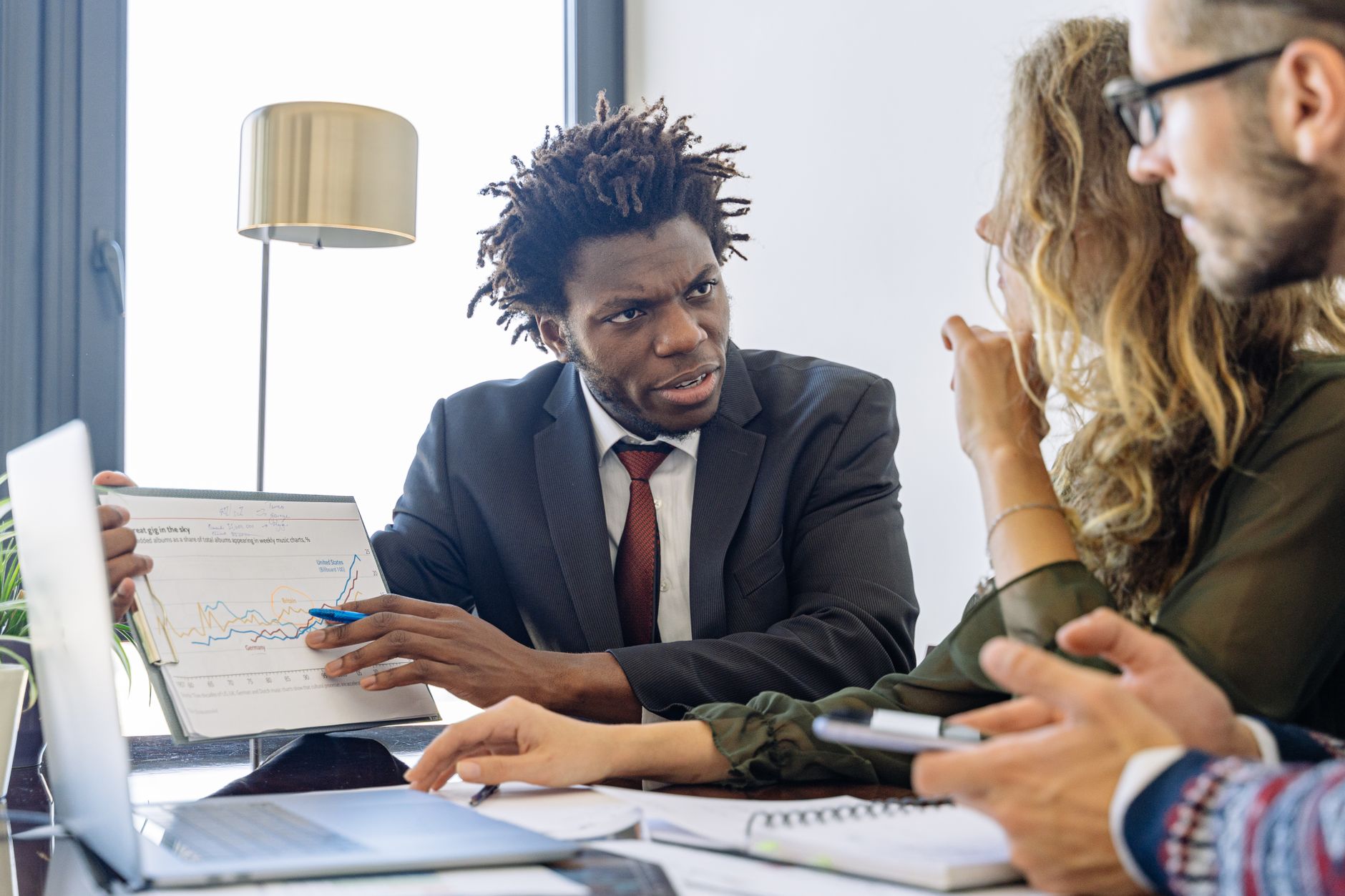A man presents financial data on a chart to attentive colleagues at a meeting