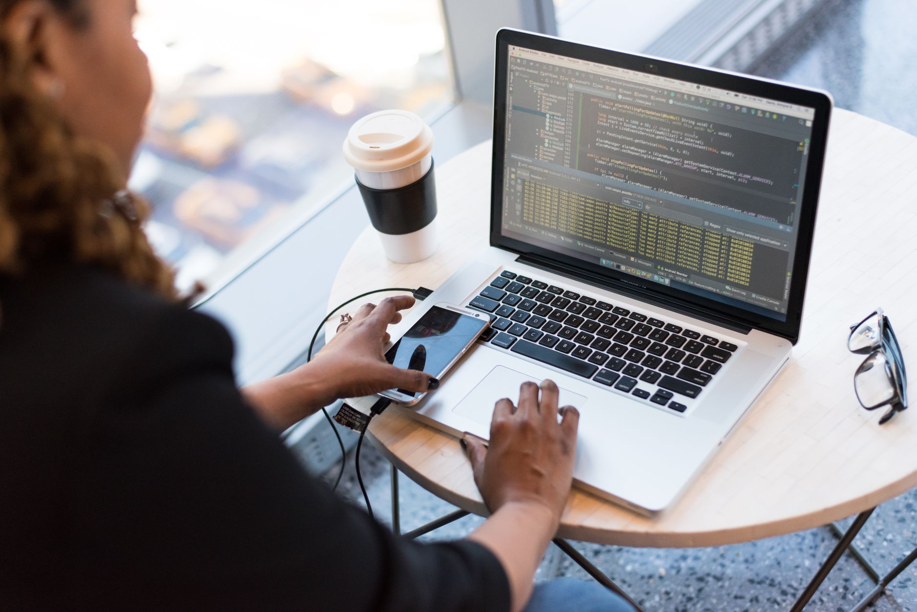 Person coding on a laptop with a smartphone, symbolizing fintech development and compliance