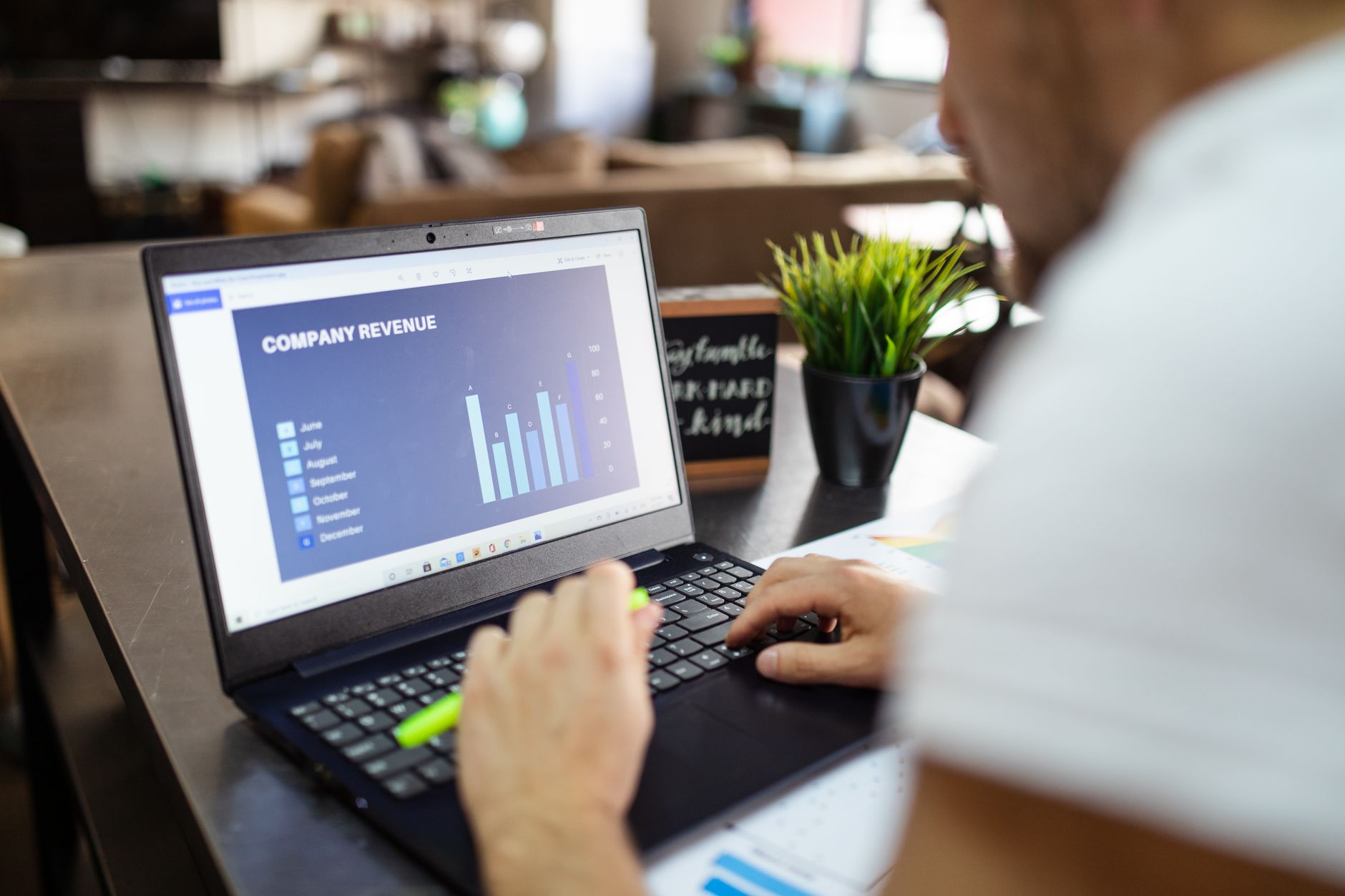 Person typing on a laptop displaying a "Company Revenue" bar chart spreadsheet
