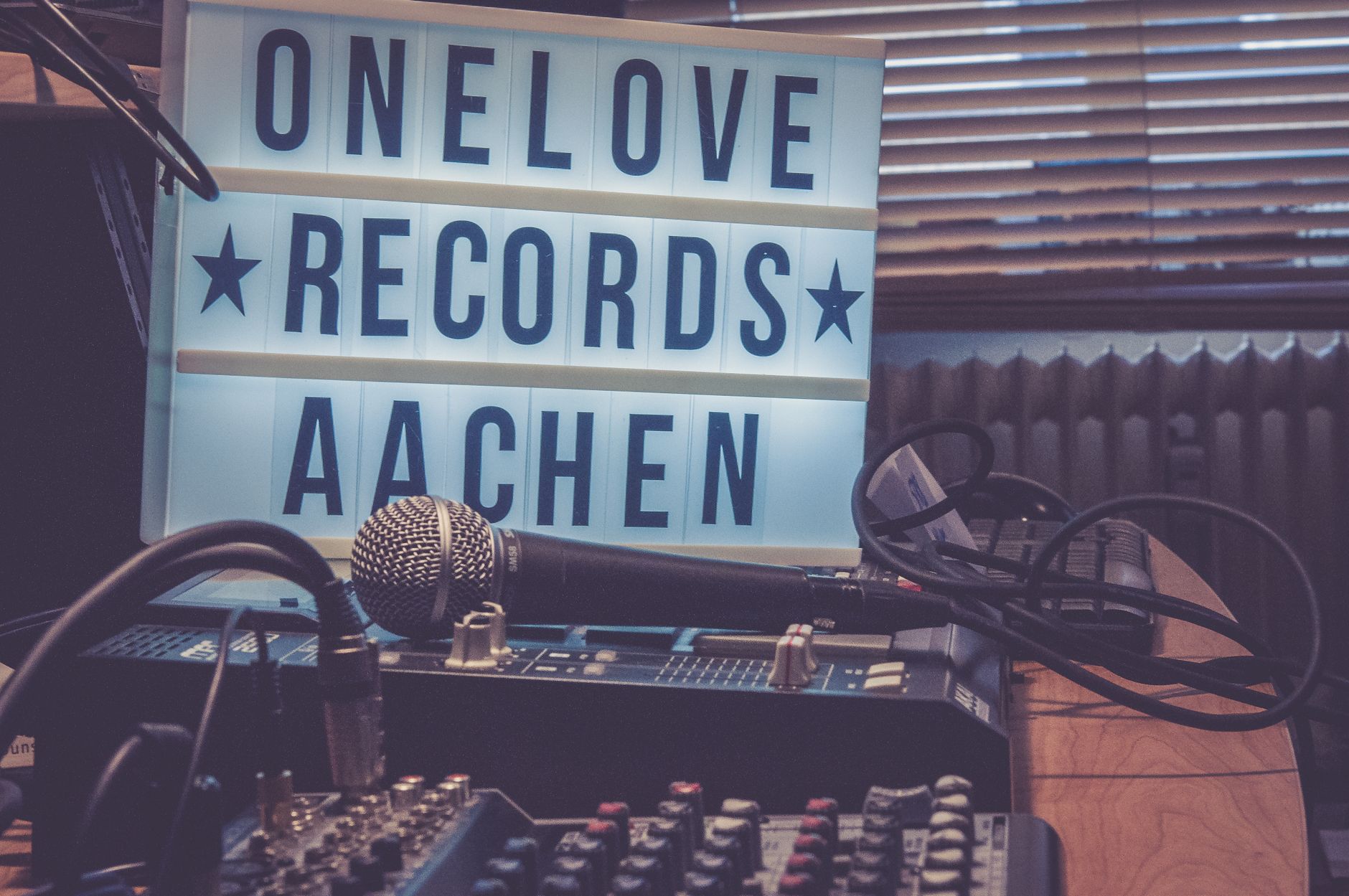 A microphone and audio mixer in front of a lightbox displaying "Onelove Records Aachen