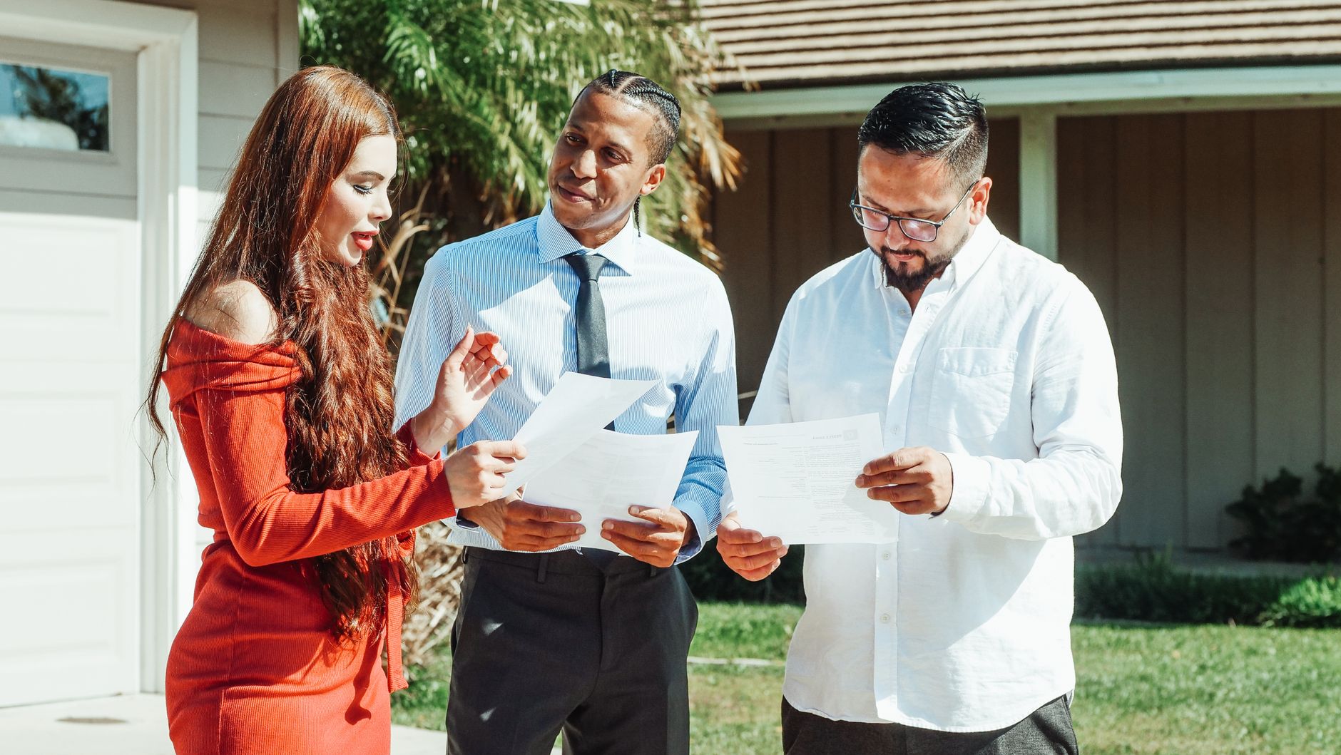 Three people discussing documents outdoors, likely for property acquisition