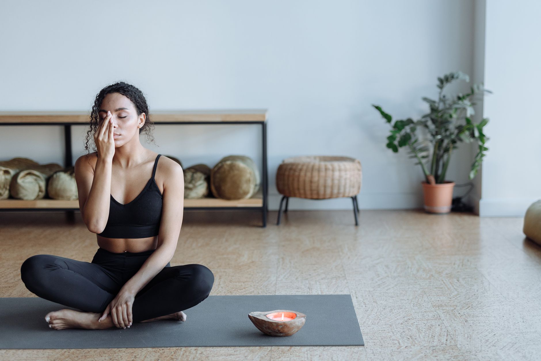 A woman meditates in a yoga pose with a lit candle for self-trust coaching
