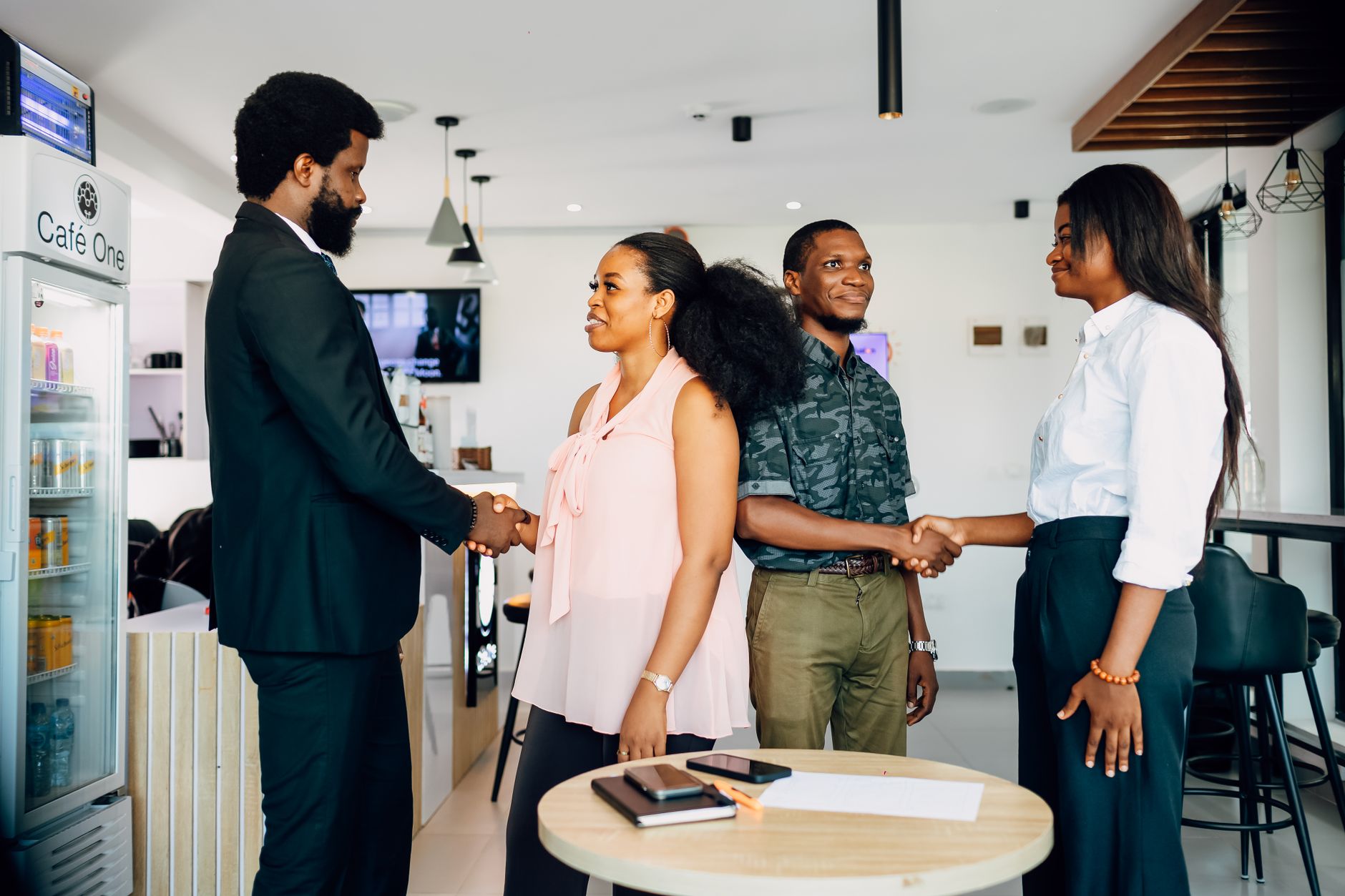 Four business people shaking hands in a bright cafe setting