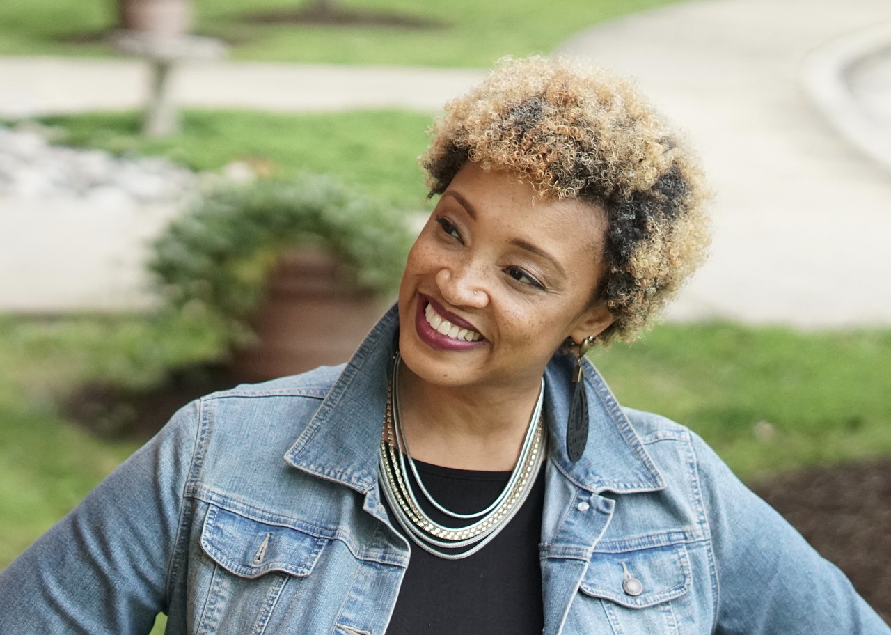 Smiling woman with curly hair looking away, wearing a denim jacket and necklace