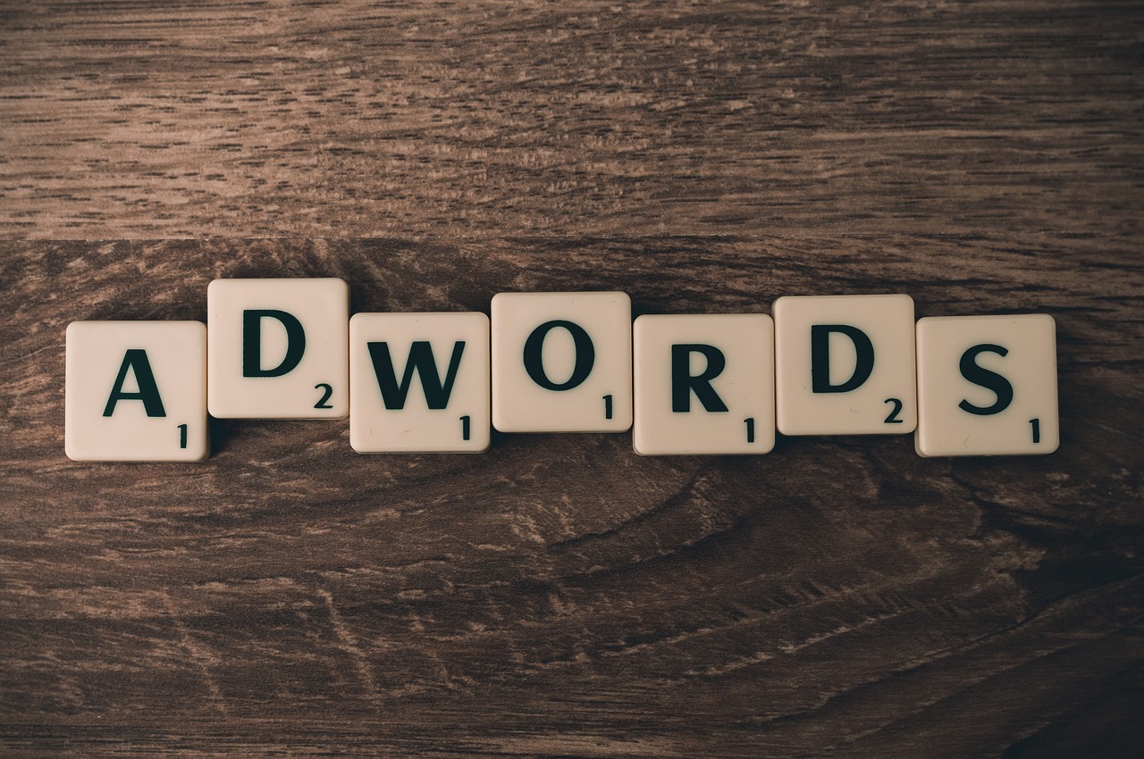 Scrabble tiles spelling "ADWORDS" on a dark wooden background, representing advertising strategies