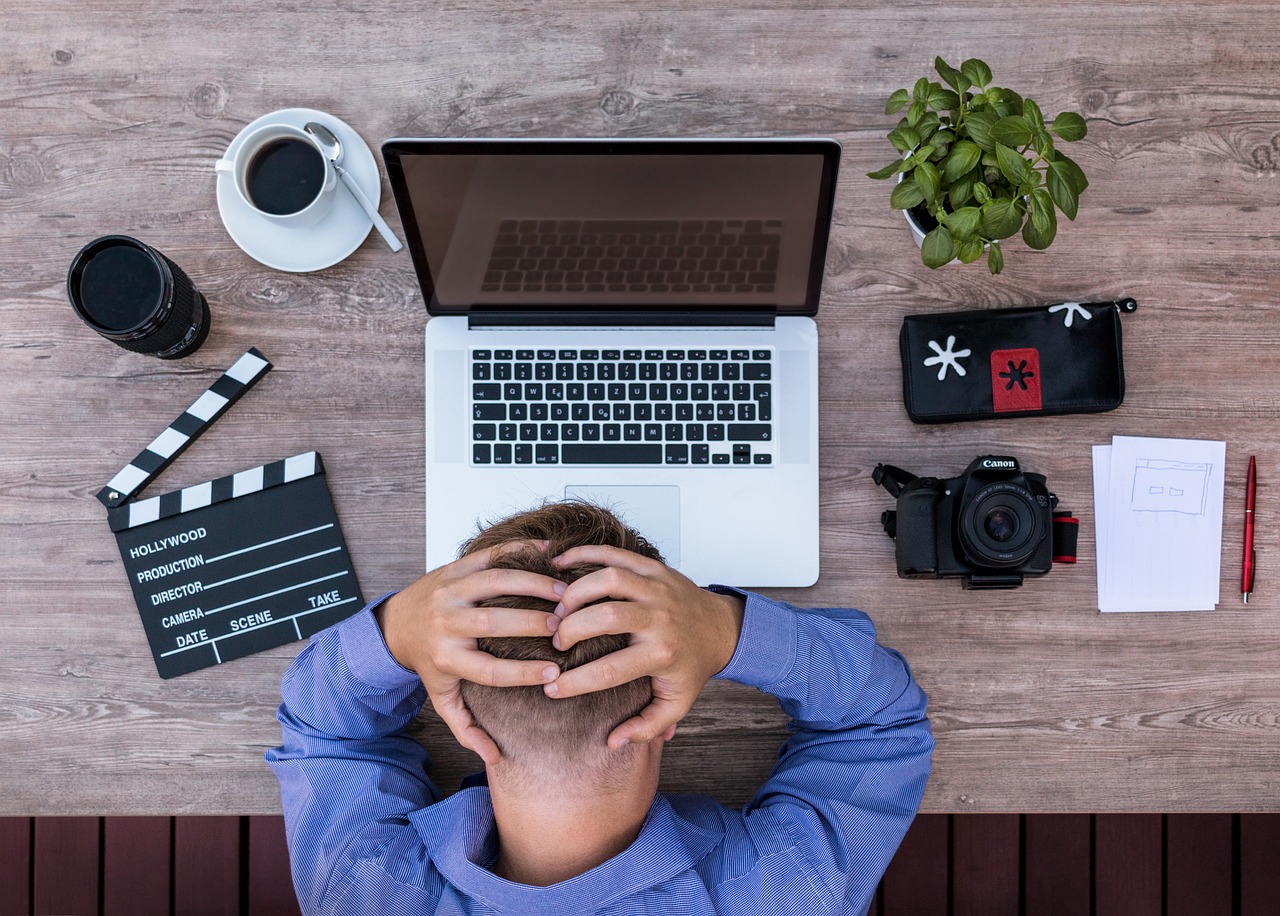 Person with hands on head, stressed by work, surrounded by laptop and creative tools