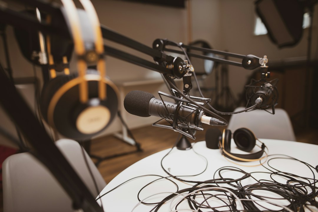 Several microphones on boom arms with headphones and tangled cables on a white table