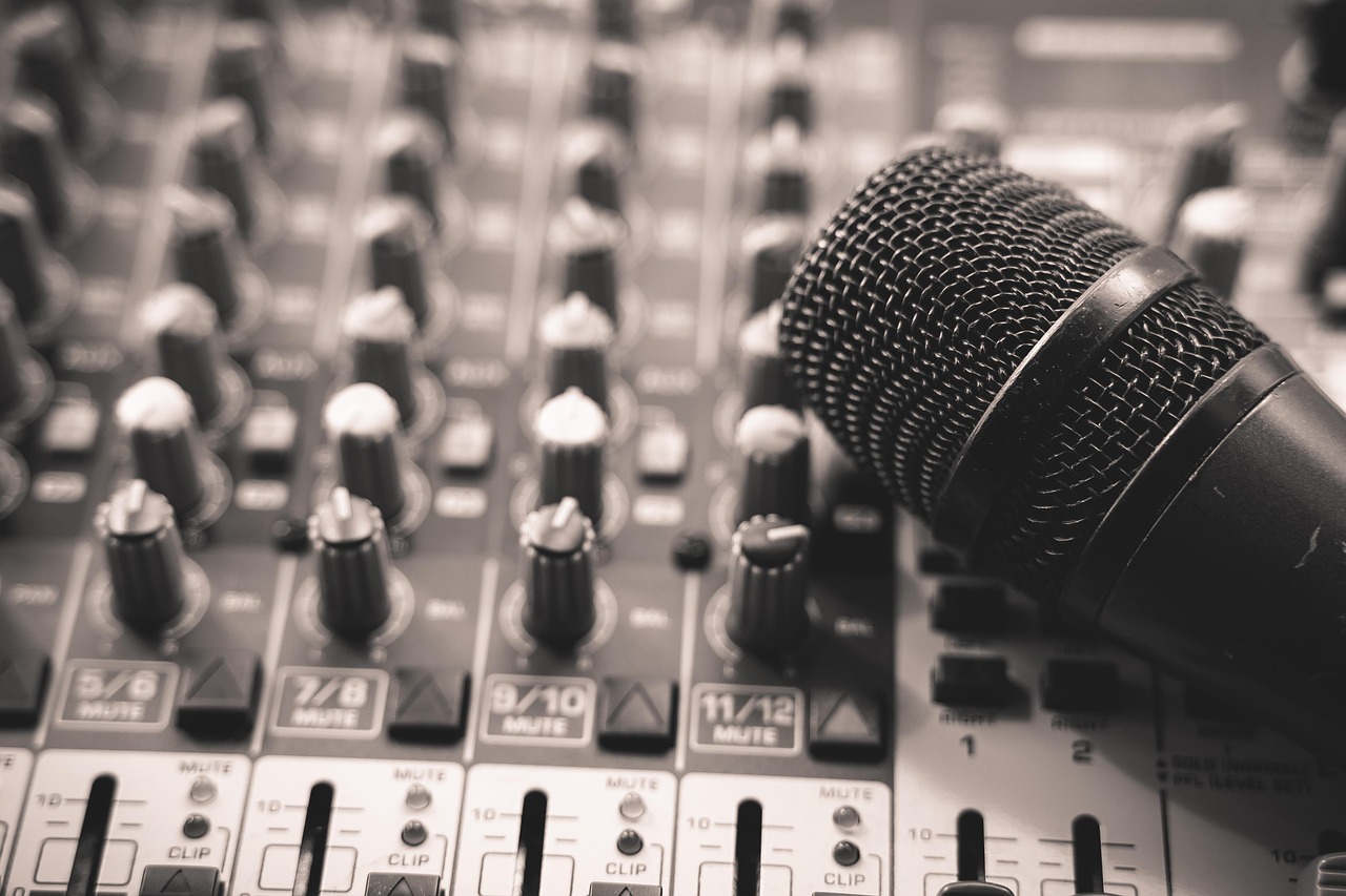 A microphone rests on an audio mixing board with many knobs and faders