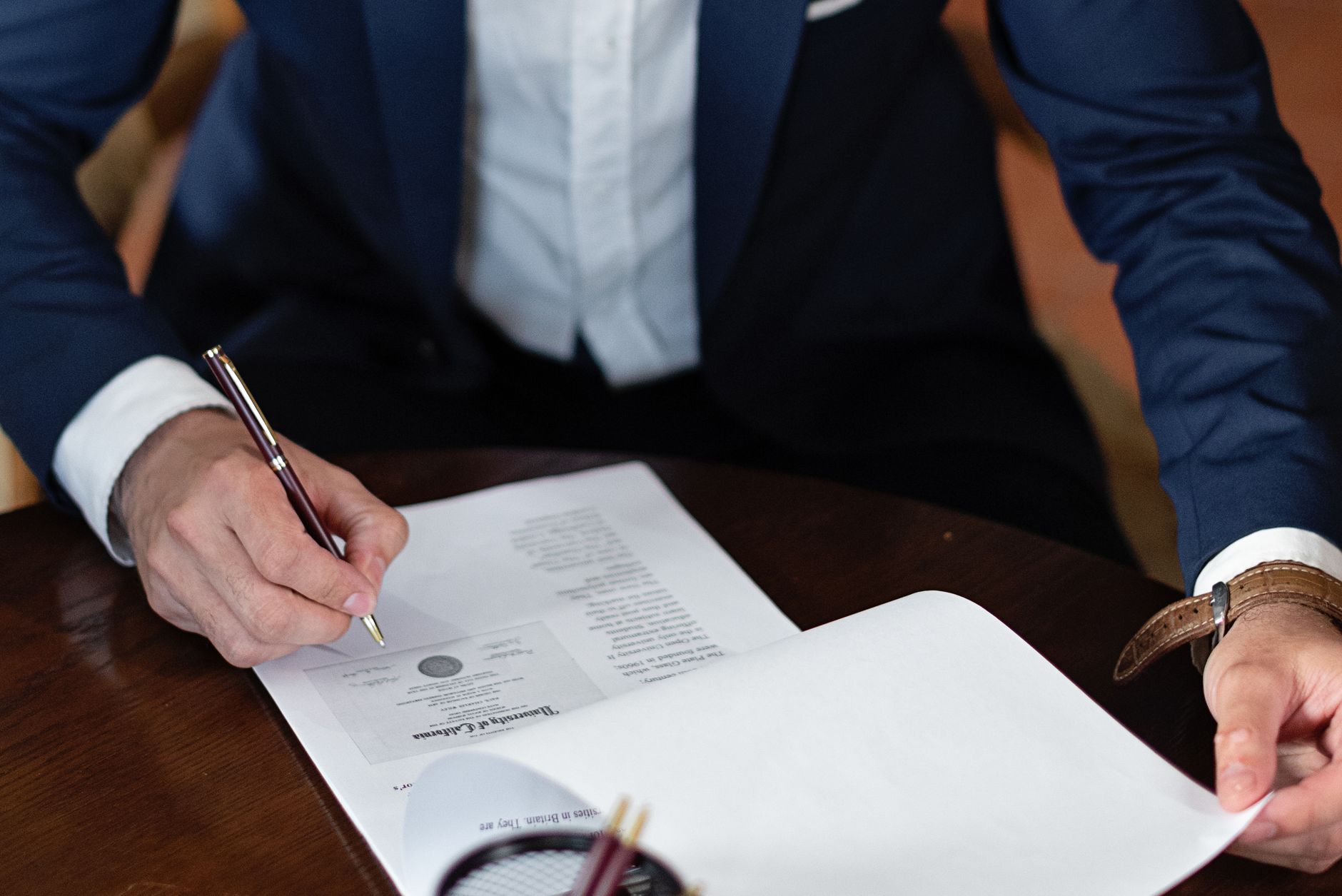 A person in a blue suit signs official documents with a pen