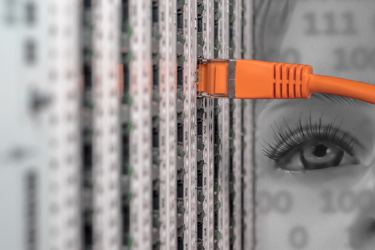 An orange ethernet cable connects to a server rack beside a faint eye
