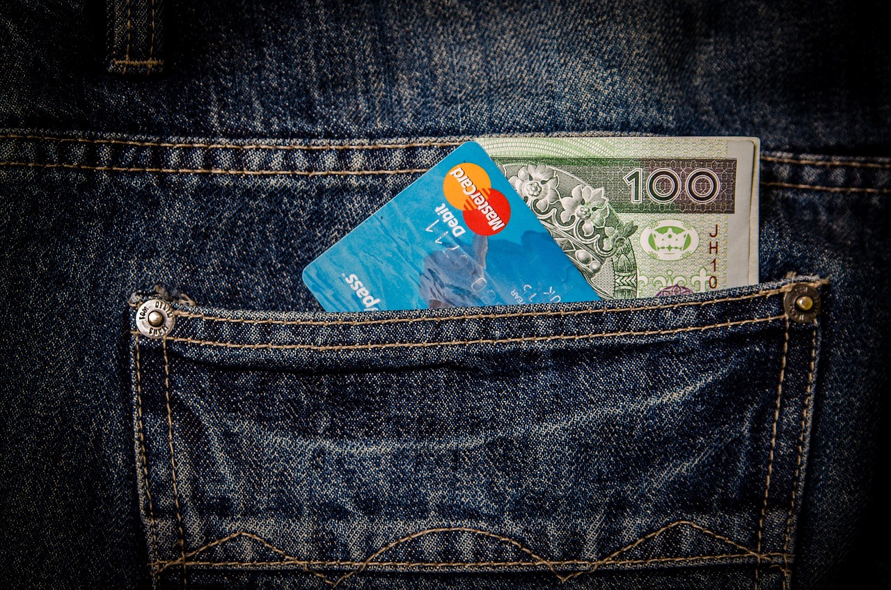 A debit card and banknote peek from a blue jean pocket, representing forgotten costs