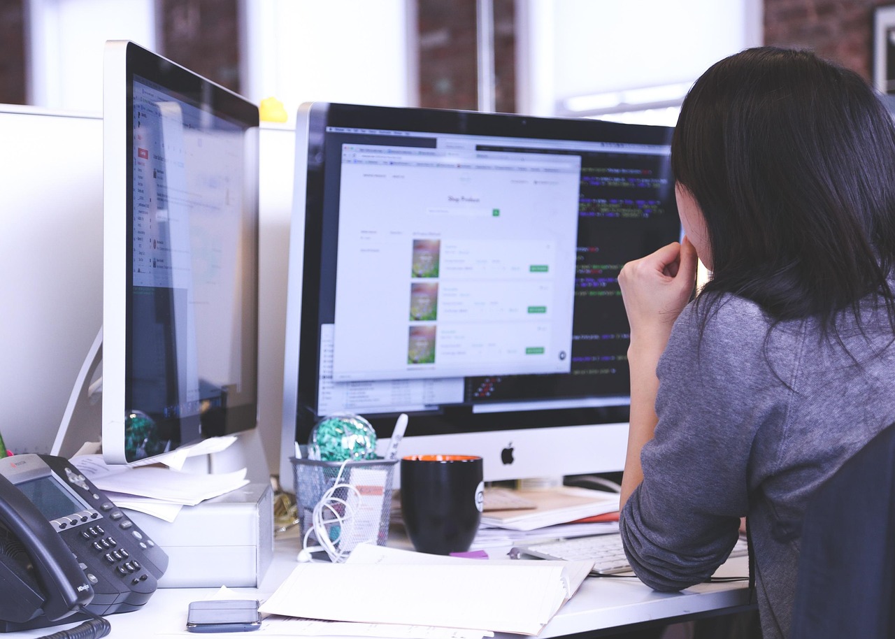 Person working at a desk with two computer monitors displaying data and code