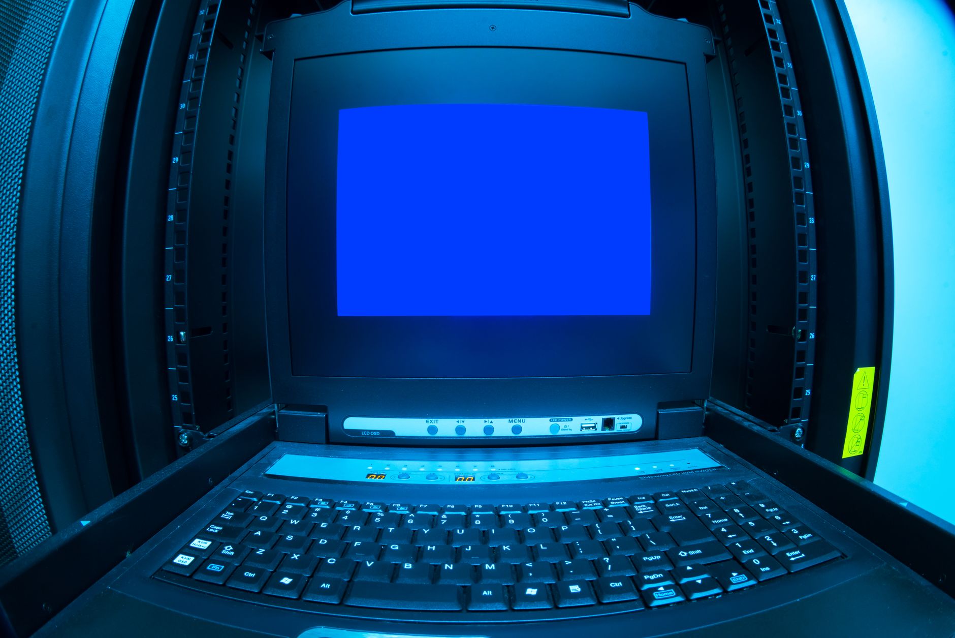 A server rack console holds a keyboard below a bright blue monitor