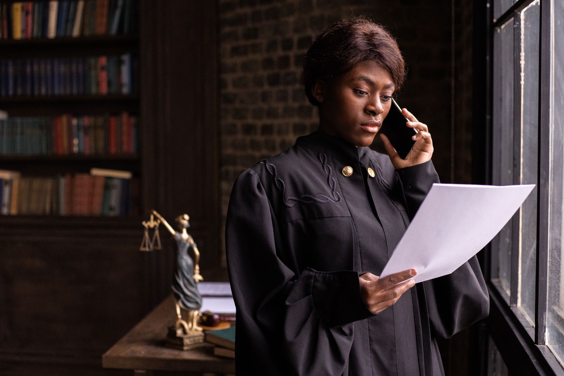 African legal consultant on phone holding documents, Lady Justice statue in background
