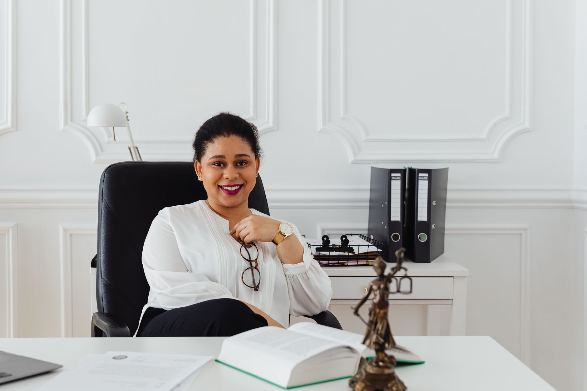 Smiling African legal consultant at her office desk with scales of justice statue