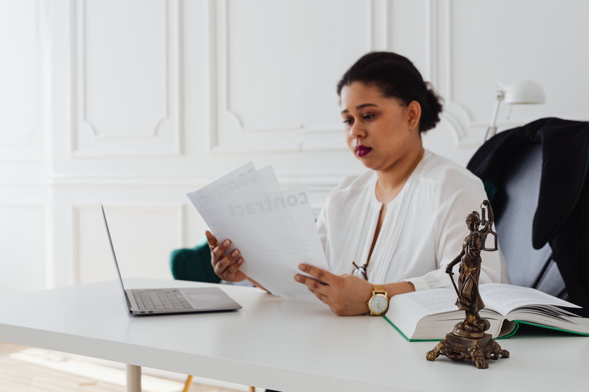 A female lawyer reviews documents at her desk with a laptop and Lady Justice statue