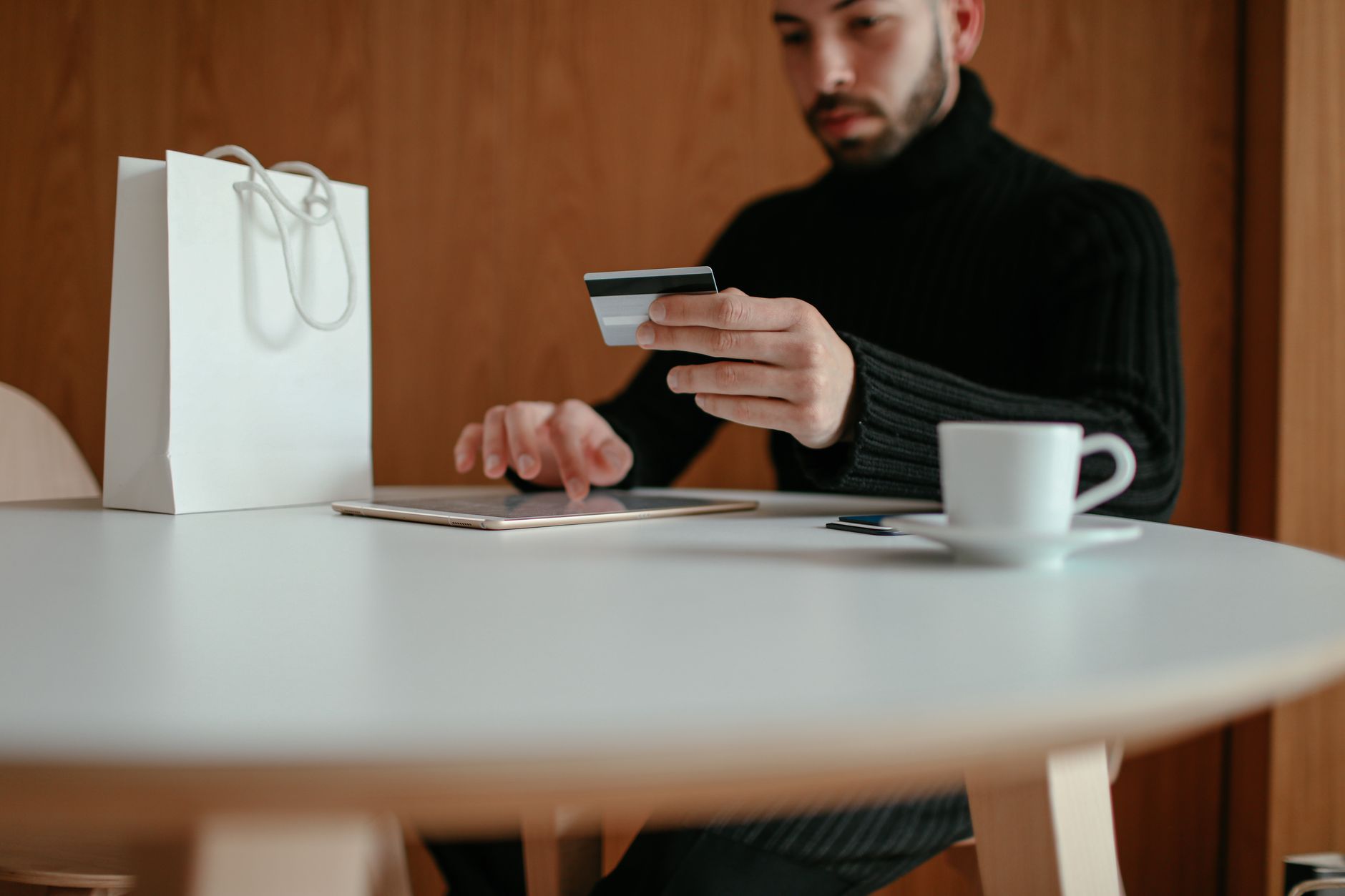 A man holds a credit card while using a tablet at a table
