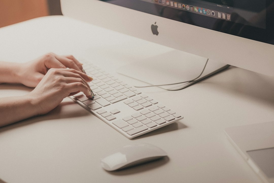 A person types on a white keyboard in front of a desktop computer