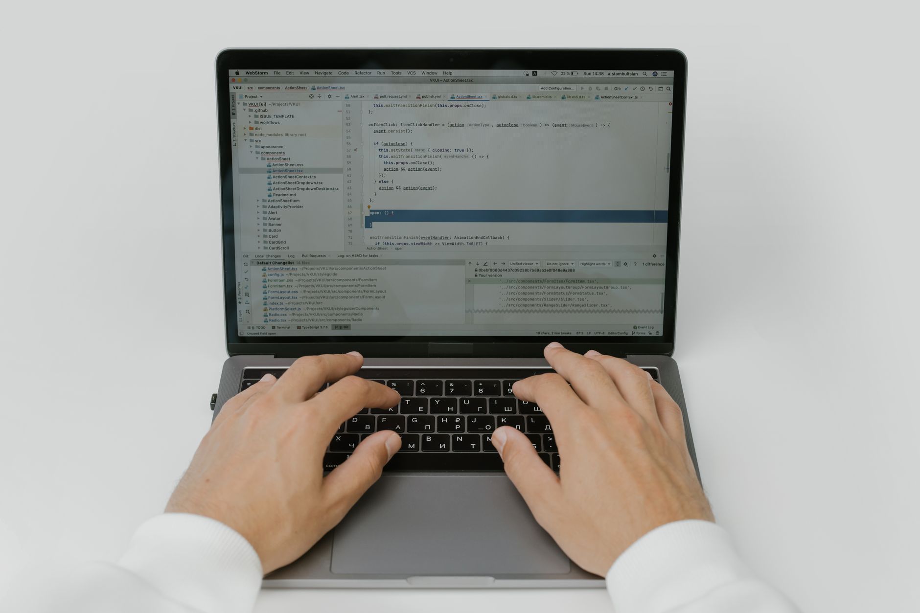 A person types on a laptop keyboard with programming code on the screen